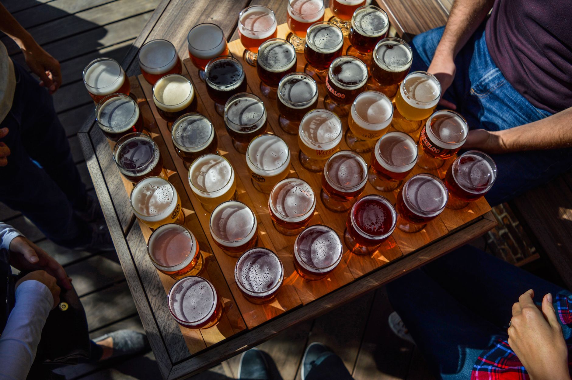 From above of crop anonymous group of friends relaxing in cafe at wooden table with many glasses of various types of beer